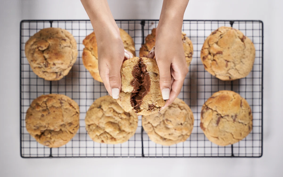 Hands splitting a chocolate-filled cookie over a cooling rack of cookies