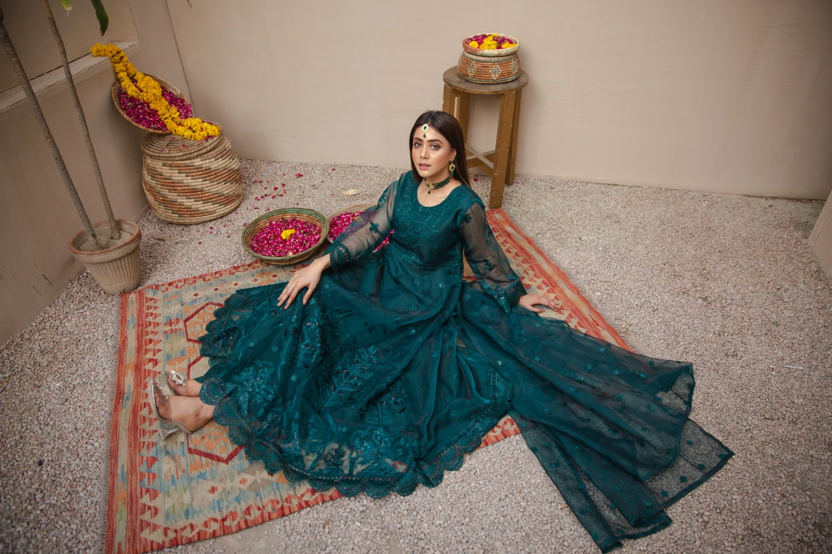Model wearing a teal embroidered outfit among baskets of flowers