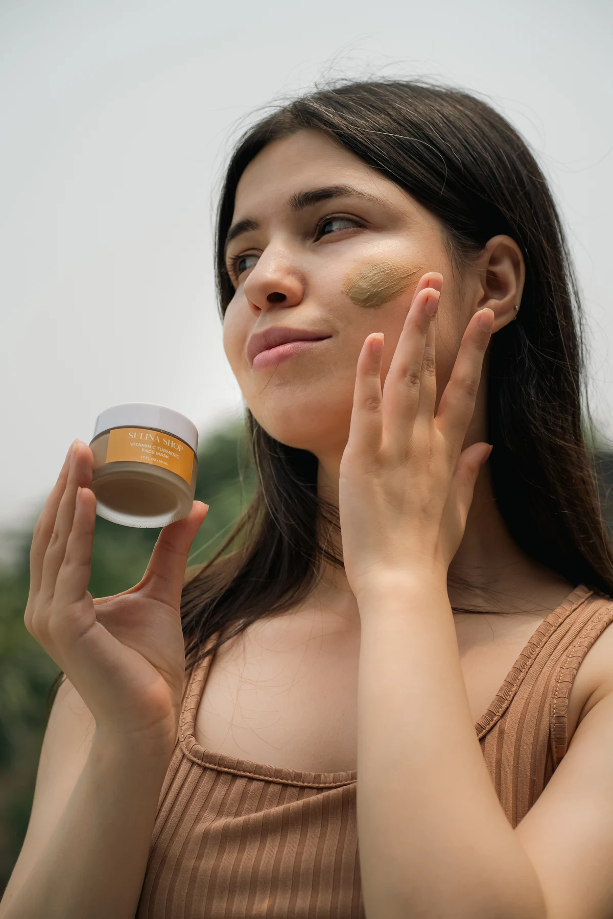 Model applying a Sulina Shop face mask outdoors